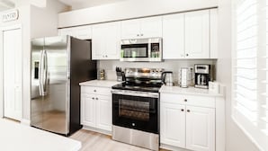 A modern kitchen with white cabinets, stainless steel appliances including a refrigerator, microwave, and oven, and a coffee maker on the countertop.