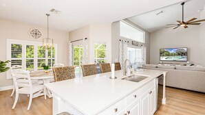 A modern kitchen with white cabinetry, a large island, and a dining area with white chairs.