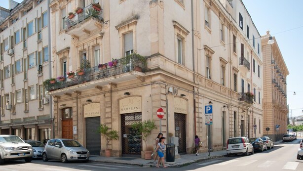 A multi-story building with a ground-floor entrance, a sign reading "MAHARANI," and a parking sign. - Harmony Central (Lecce)