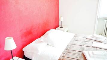 Ein Hotelzimmer mit roter Akzentwand, einem ordentlich bezogenen Bett mit weißen Leinentüchern und einem Nachttisch mit Lampe.