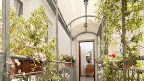 A narrow corridor with artificial green turf, potted plants on both sides, and a metal railing. - Harmony Central (Lecce)
