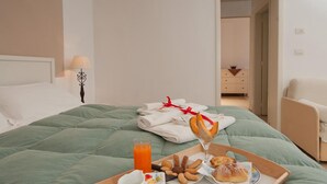 A neatly made bed with a green bedspread, a tray with breakfast items including pastries, a glass of orange juice, and a cup of coffee. - Harmony Central (Lecce)