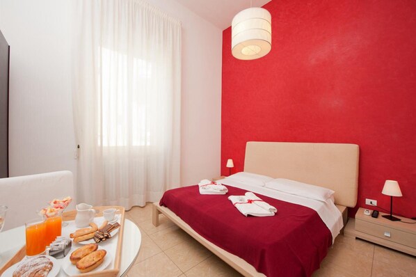 Une chambre d’hôtel avec un lit, un plateau de petit-déjeuner, une table de chevet et un mur rouge.