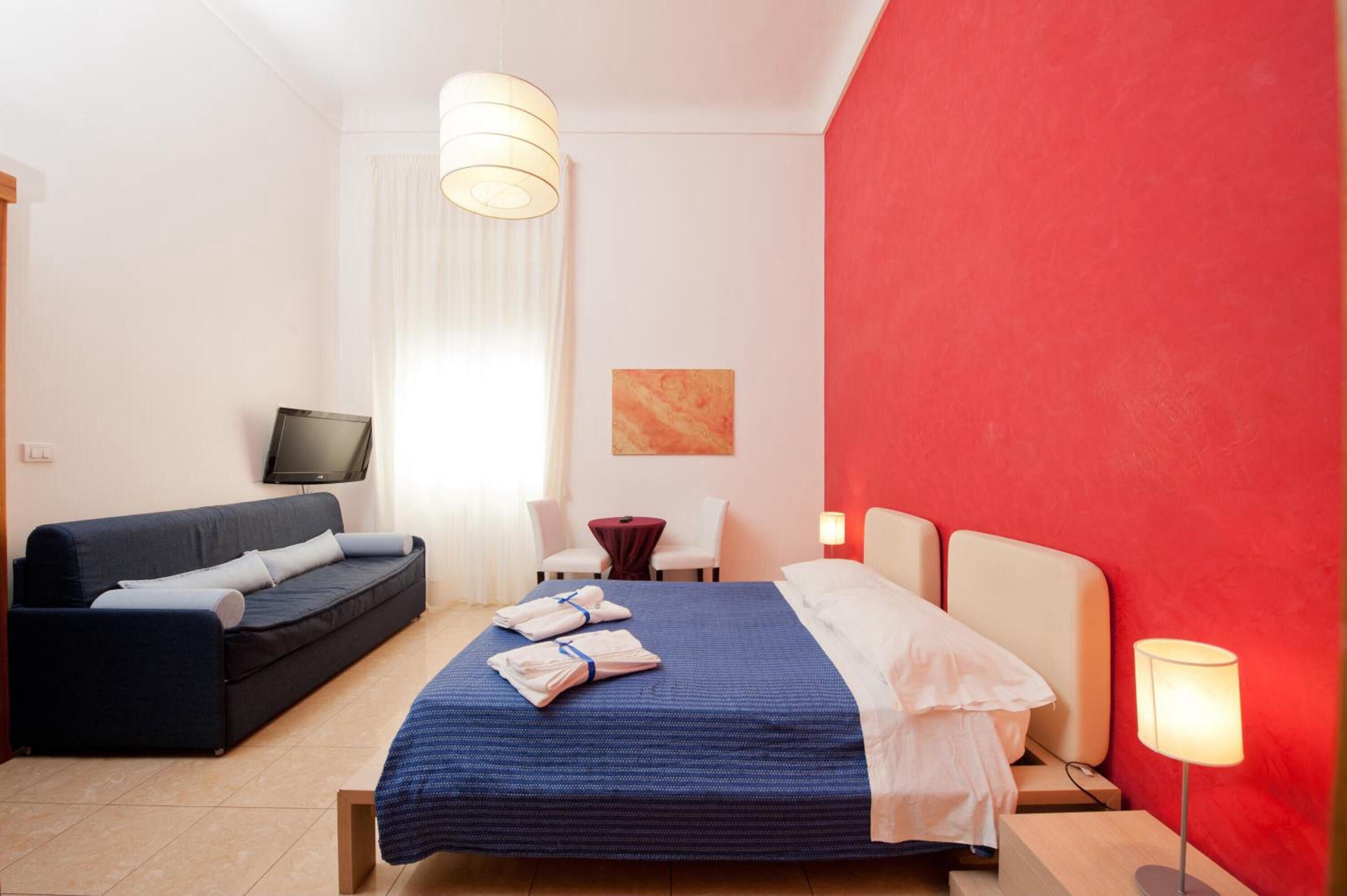 Una habitación de hotel con cama, sofá, televisión, escritorio y lámpara.