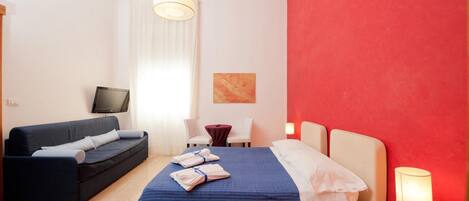 Una habitación de hotel con cama, sofá, televisión, escritorio y lámpara.