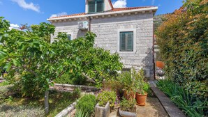 A stone building with a tiled roof, a small attached structure, and a garden with various plants and a wooden deck. - Dubrovnik art Gateway (Dubrovnik)