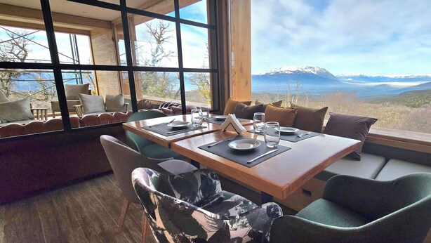 Un comedor con mesa de madera preparada para dos personas, ventanas amplias que ofrecen vistas a la montaña y asientos acolchados.