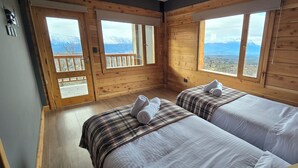Habitación tipo cabaña de madera con dos camas, un balcón y vista a la montaña.