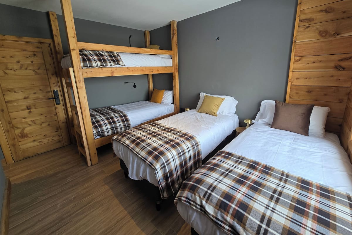 A room with a bunk bed, two single beds, wooden walls, and a wooden floor.