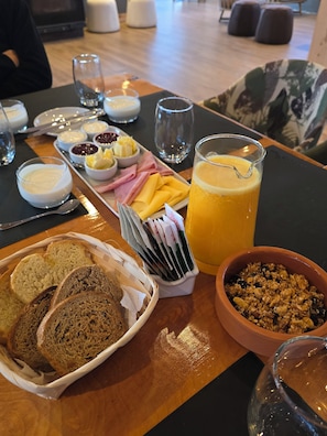 A breakfast setting with bread, cheese, ham, fruit, and a glass of orange juice on a table. - Après Ski Lodge de Montaña (El Bolson)