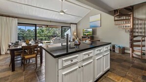 Een moderne keuken met een centraal eiland, een eethoek met stoelen, een groot raam met uitzicht en een trap.