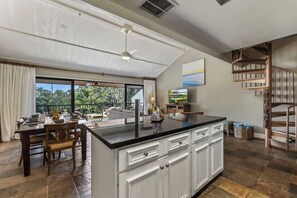 Eine moderne Küche mit einer zentralen Kochinsel, Essbereich mit Stühlen, einem großen Fenster mit Ausblick und einer Treppe.
