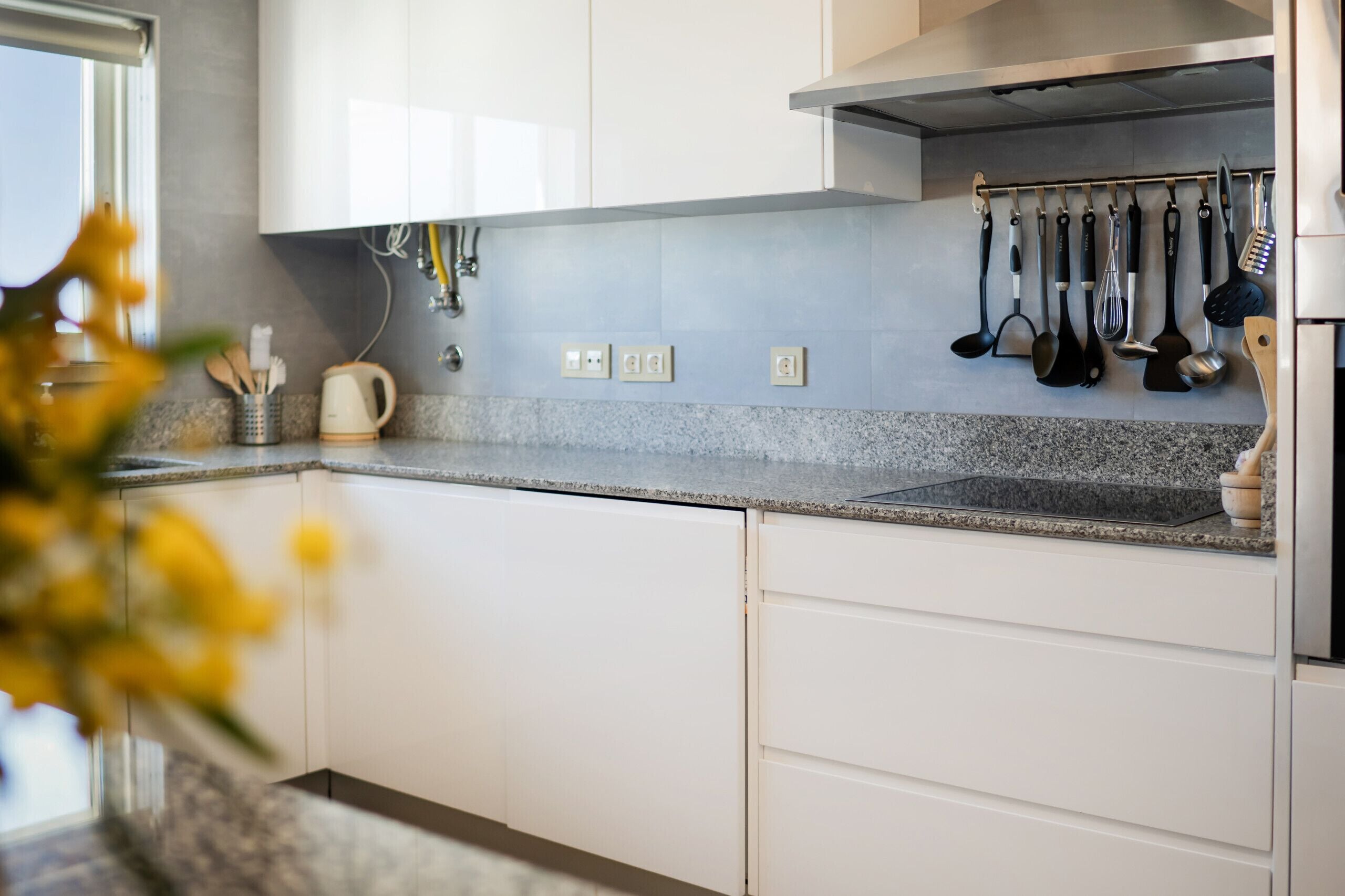 Una cocina moderna con armarios blancos, encimera de granito y diversos utensilios de cocina colgados en la pared.
