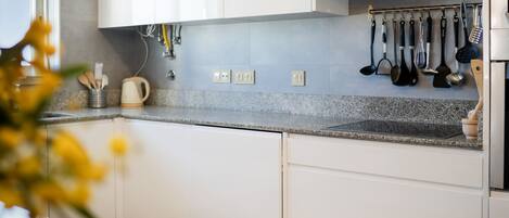 Una cocina moderna con armarios blancos, encimera de granito y diversos utensilios de cocina colgados en la pared.
