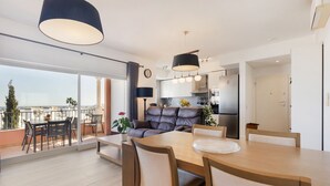A modern apartment with a dining area, a sofa, a balcony with a table and chairs, and a kitchen in the background. - Apt. Deluxe OCV - Pool & Albufeira View (Albufeira)