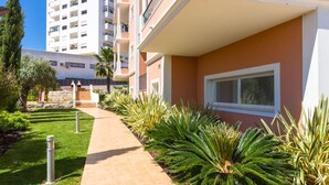 A pathway leading to a building with a balcony, surrounded by well-maintained greenery and a tall residential building in the background. - Apt. Deluxe OCV - Pool & Albufeira View (Albufeira)