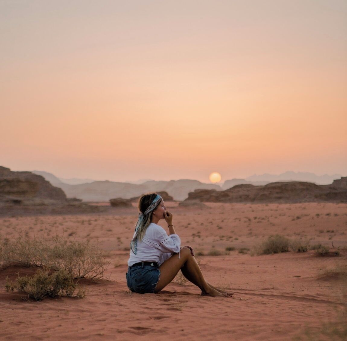 A person sitting on the ground in a desert landscape during sunset.