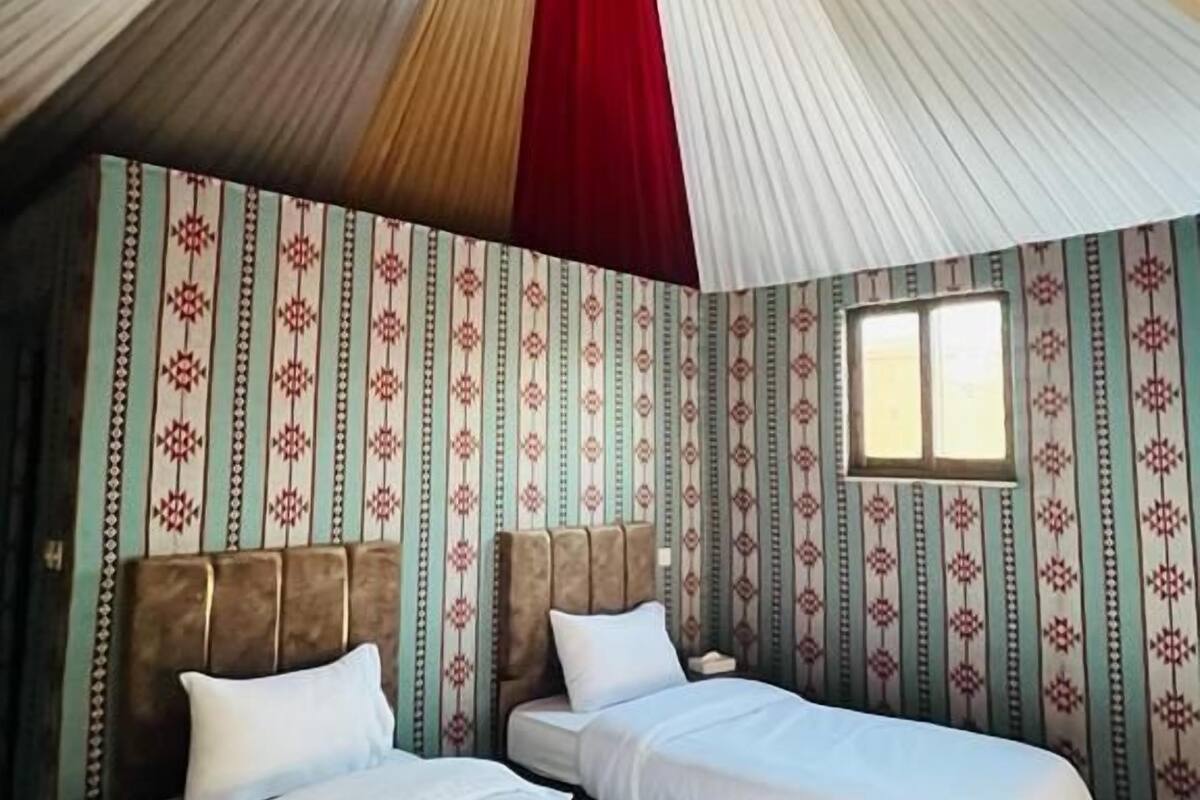 A room with two beds, patterned wallpaper, and a unique ceiling design.