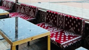 A room with a large window offering a view of a desert landscape with tents. There are cushioned seating areas and a glass table. - Star Wars Wadi Rum  (Wadi Rum)