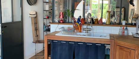 A modern kitchen with a wooden countertop, a sink, and a mirror above it. There is a wooden cabinet to the right and a black door to the left.