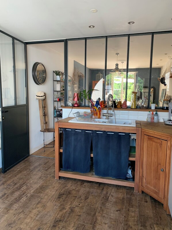 A modern kitchen with a wooden countertop, a sink, and a mirror above it. There is a wooden cabinet to the right and a black door to the left.