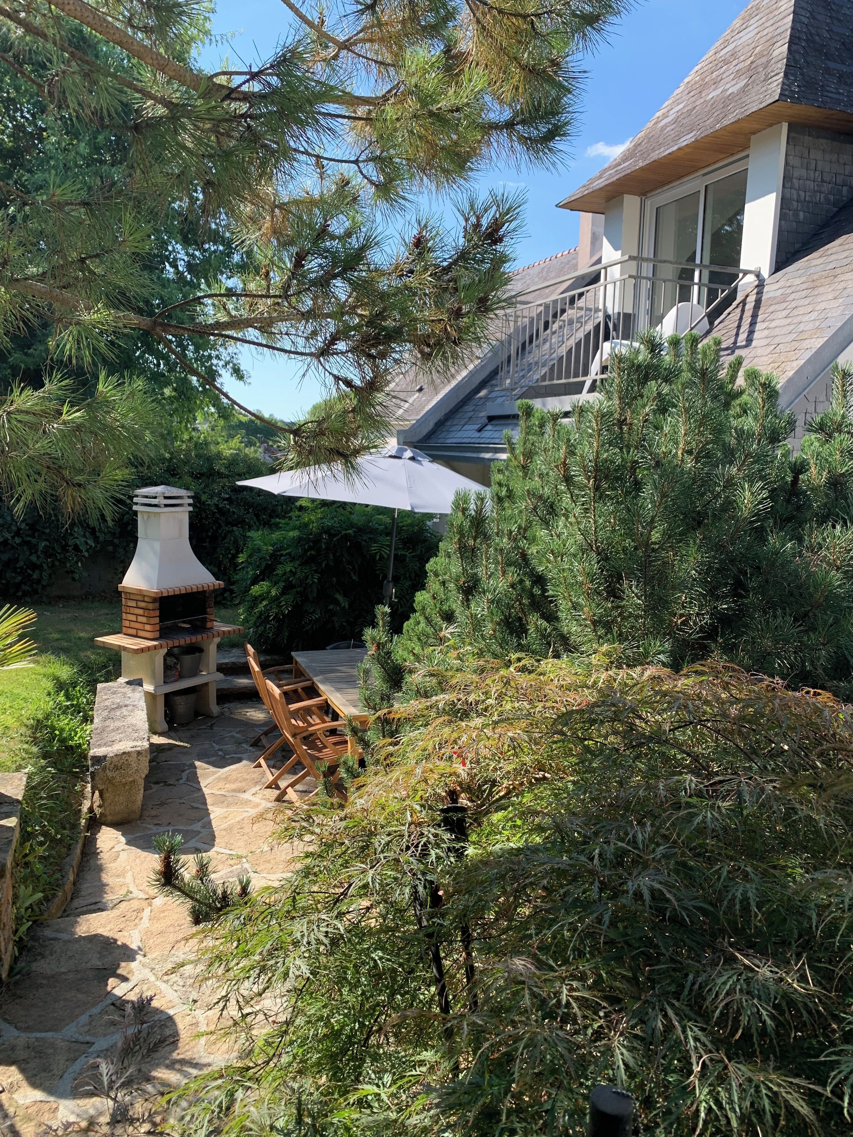 A backyard with a stone barbecue grill, wooden deck, and a covered patio area.