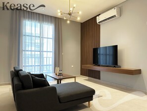 Relax in this stylish living room with a large flat-screen TV, dark grey sofa, and glass coffee table.