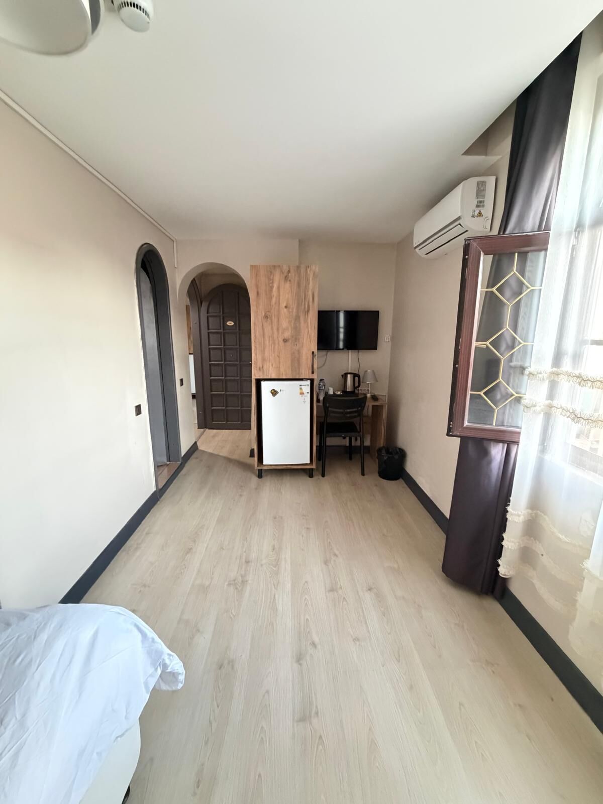 A room with a bed, a small kitchenette, a TV, and a window with curtains.