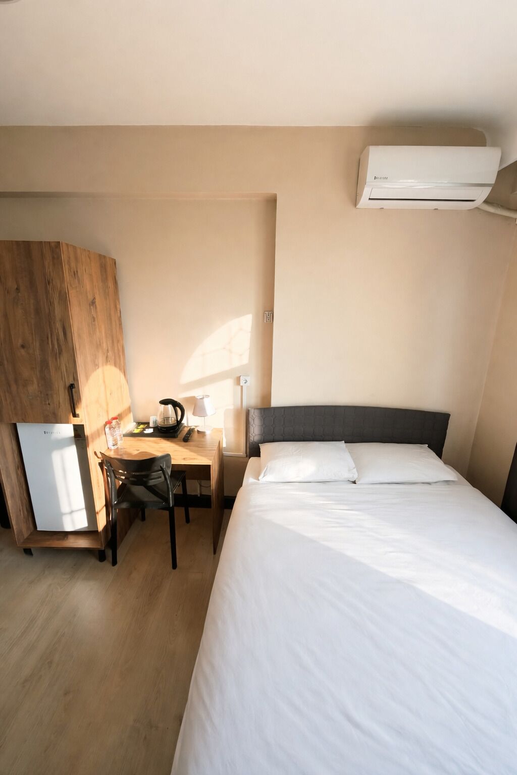 Een hotelkamer met een bed, een bureau, een stoel, een koelkast en een airconditioner.