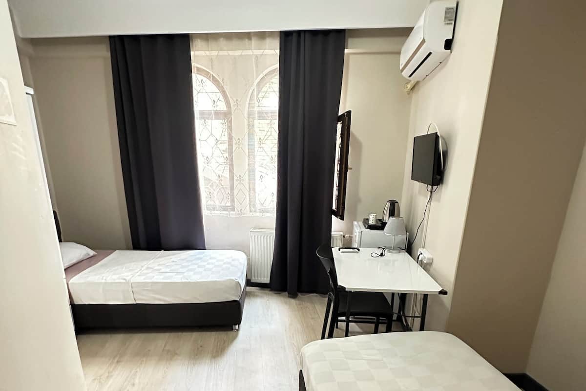 Ein Hotelzimmer mit zwei Einzelbetten, einem Schreibtisch mit Stuhl, einem Heizkörper und einem Fenster mit Vorhängen.