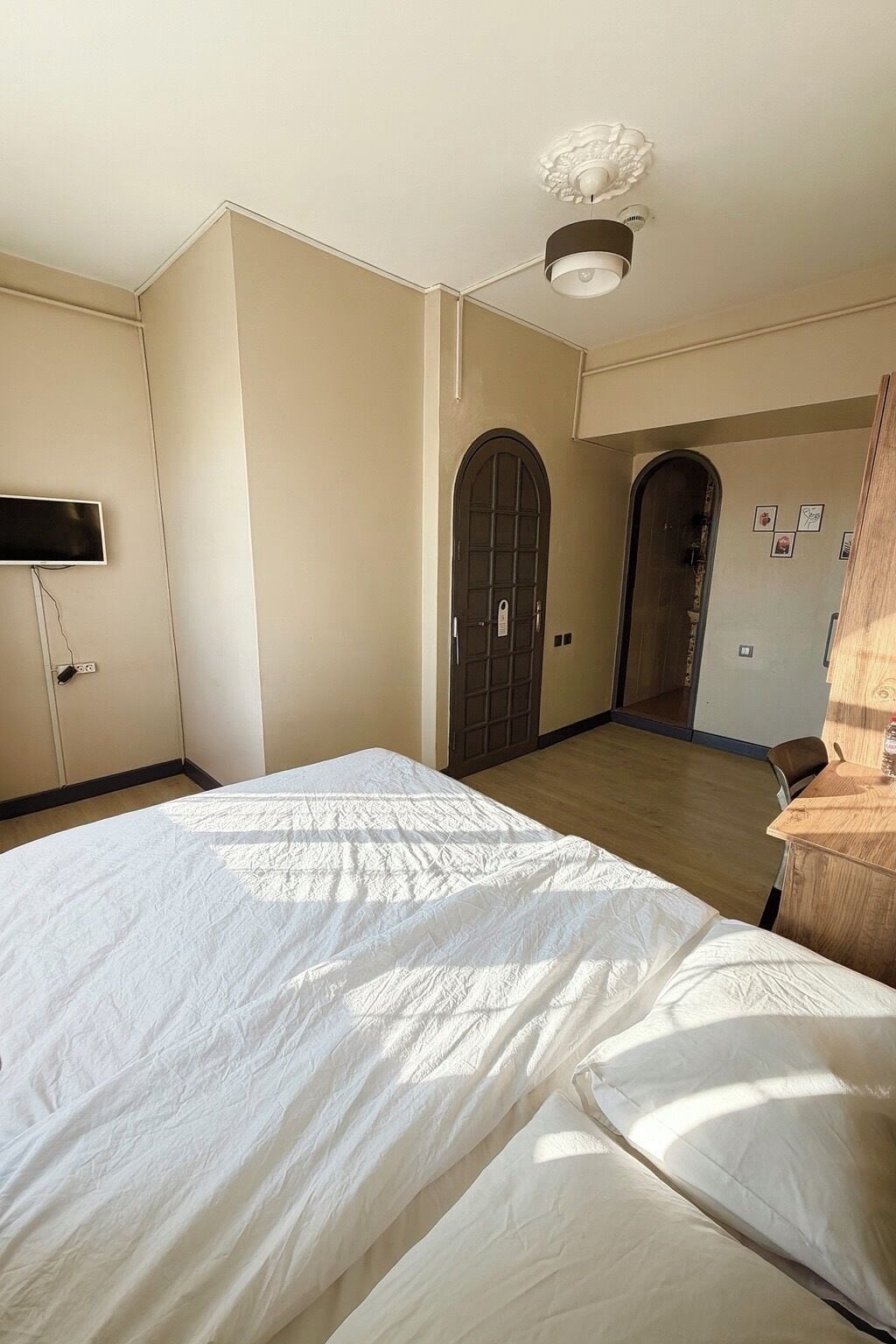 A hotel room with a large bed, a flat-screen TV mounted on the wall, a ceiling fan, and a door leading to another room.