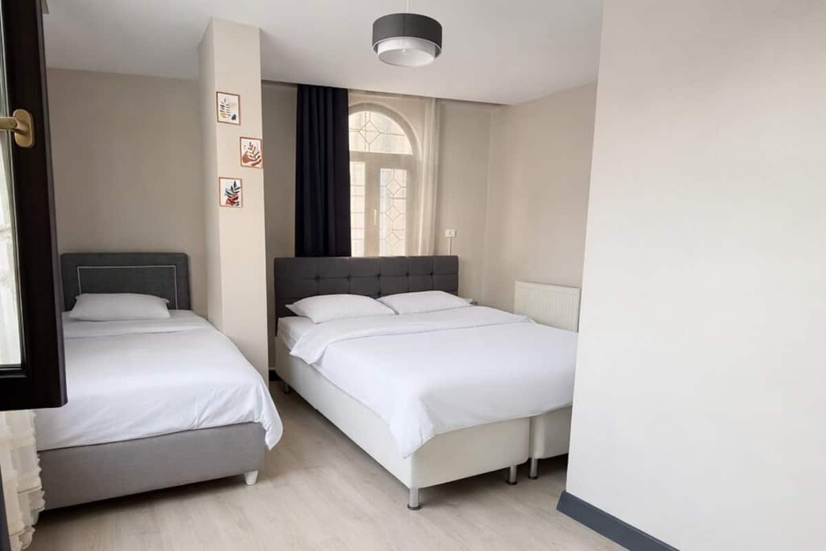Ein Hotelzimmer mit zwei Betten, einem Fenster mit Vorhängen, einem Deckenventilator und einer Lampenleuchte.