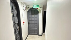 Un corridoio con una porta grigia, un segnale di uscita verde e un muro bianco.