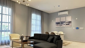 A modern living room with a sectional sofa, a small table, and a dining area in the background. - Hittin B-3 Latest Development  AX58 (Riyadh)