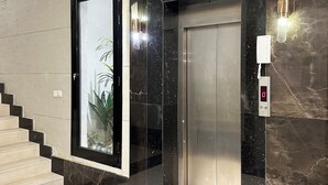 Un elevador moderno con pantalla digital, puerta de cristal con una planta y pared de mármol.