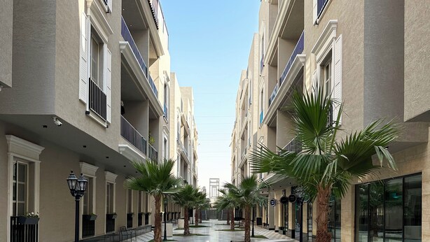 Un pasillo con piso a cuadros, palmeras y edificios con balcones.