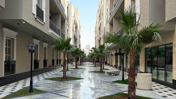 A corridor with a checkered floor, palm trees, and buildings with balconies.