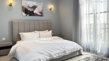 Een moderne slaapkamer met een groot bed, twee wandlampen, een schilderij en een groot raam met dunne gordijnen.
