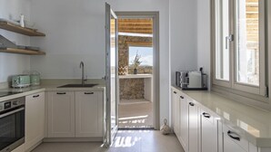 A modern kitchen with white cabinetry, a built-in oven, a sink, and a window overlooking a stone wall.