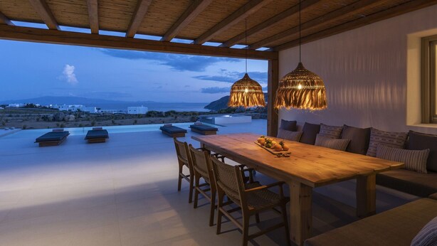 A rooftop terrace with a wooden table and chairs, a sofa, and two hanging lamps.