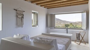 A bedroom with a large window, a bed, a bedside table, and a hanging macrame wall decoration.