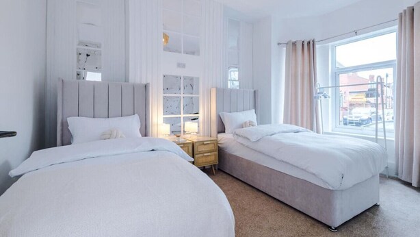 Habitación de hotel con dos camas, una mesita de noche, una ventana con cortinas y vista a la calle.