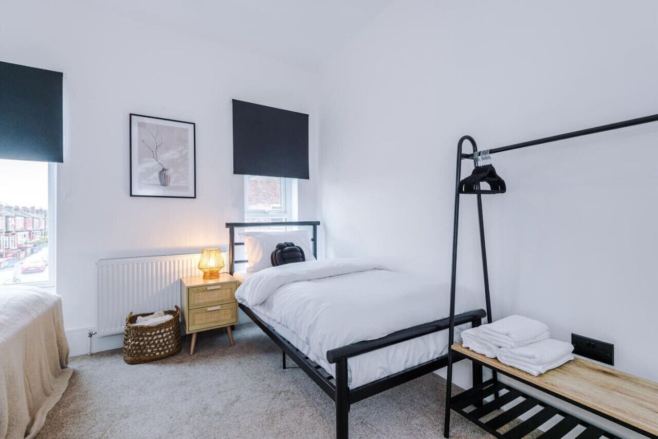 Un dormitorio minimalista con cama, mesita de noche, lámpara y vista a la ciudad por la ventana.