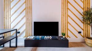 Una sala de estar moderna con un televisor negro sobre un mueble bajo, una mesa de centro negra con objetos decorativos, una pared de madera con diseños diagonales y una planta en una cesta tejida.