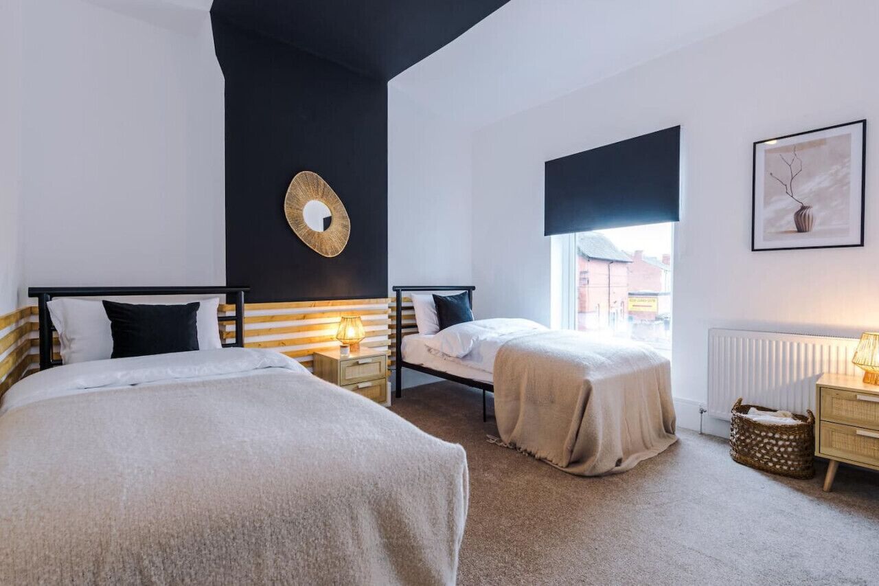 Et soveværelse med to senge, et natbord med lampe, en radiator og et billede i ramme på væggen.