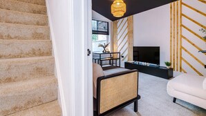 Una sala de estar moderna con una escalera, un televisor y un sillón de ratán.