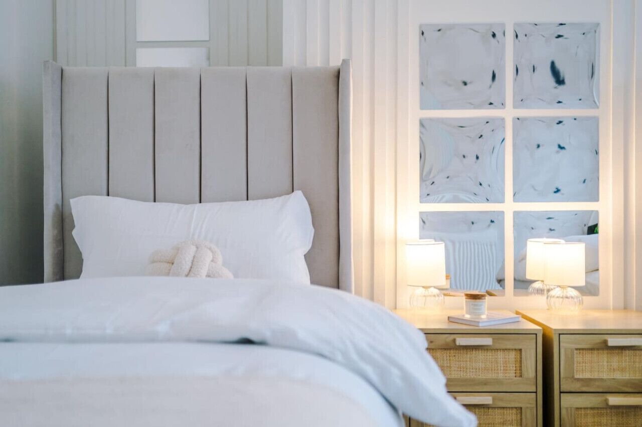 A neatly made bed with a headboard, bedside tables with lamps, and a window with a view of the sky.