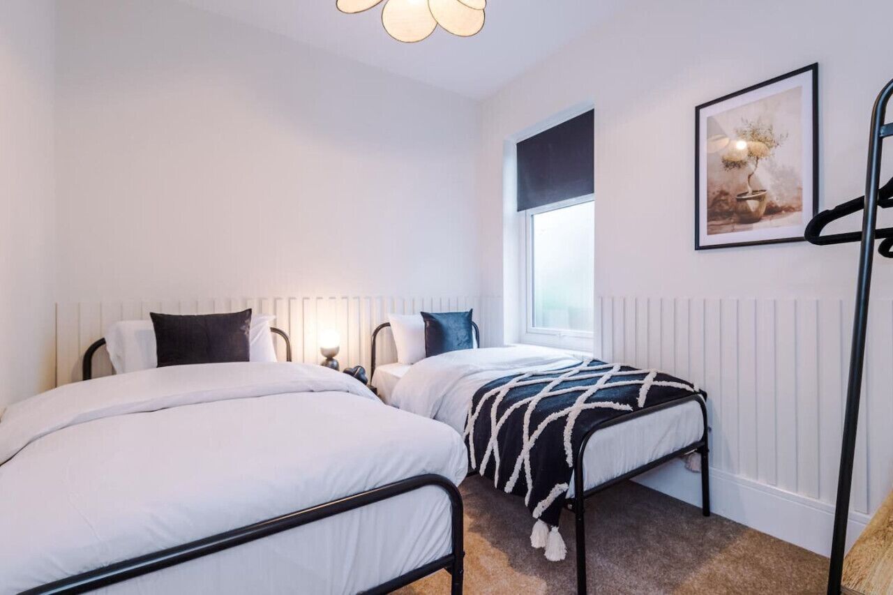A bedroom with two beds, a window, a radiator, and a framed picture on the wall.