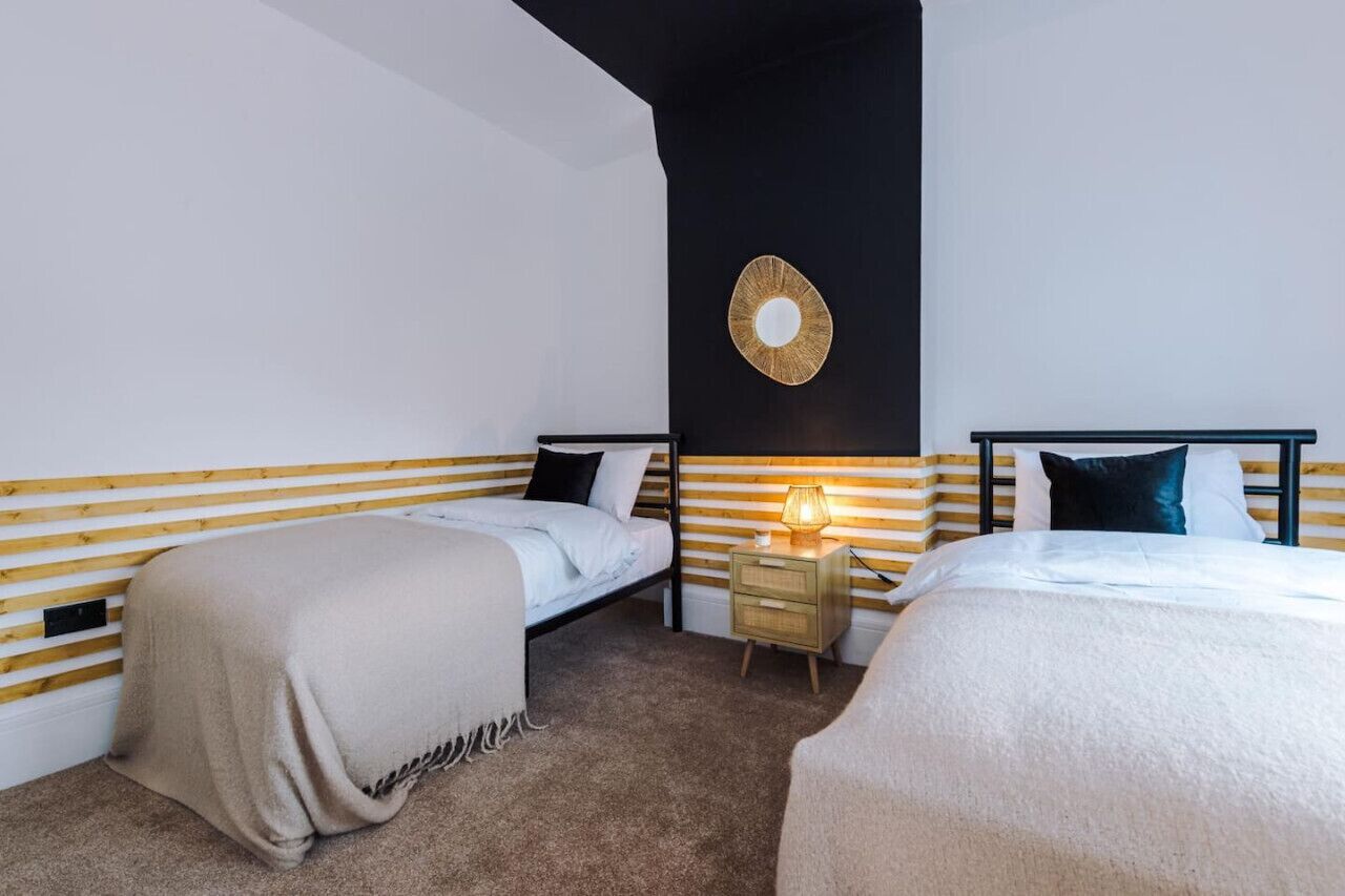 A bedroom with two beds, a bedside table with a lamp, and a wall-mounted circular light fixture.