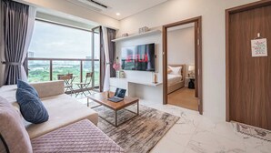 Ein modernes Hotelzimmer mit großem Fernseher, einer Couch, einem Couchtisch und einem Balkon mit Stadtblick.